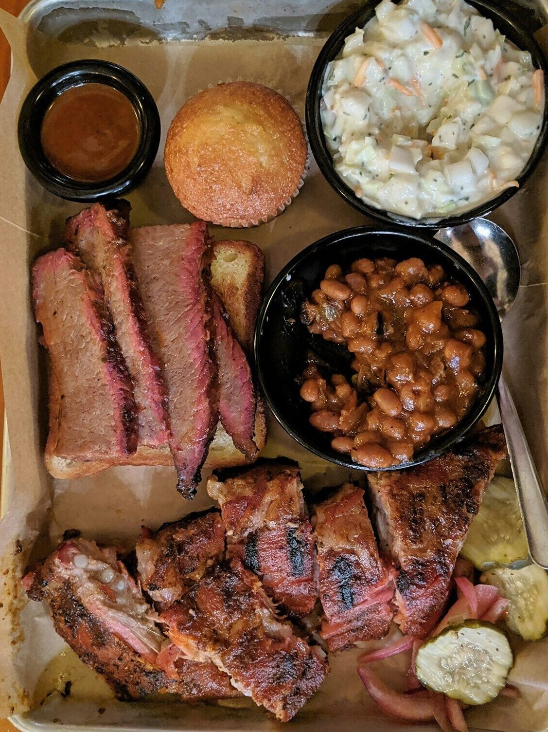 Texas-style barbecue platter with smoked ribs, brisket, baked beans, coleslaw, and cornbread — traditional Juneteenth celebration food.