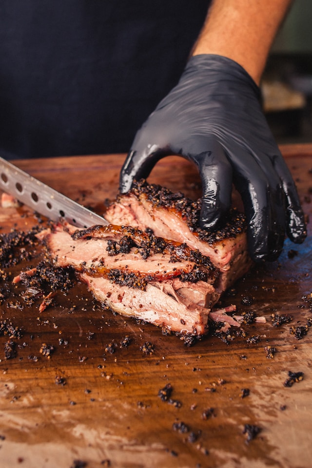 Close-up of a pitmaster slicing smoked brisket on a wooden cutting board — showcasing Texas BBQ craftsmanship.