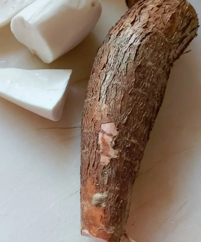 Cassava root and peeled sections on a cutting board — a starchy West African staple linked to traditional Beninese and American American food.