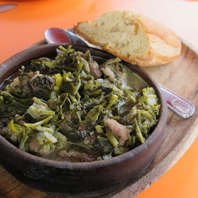 Traditional Georgian chakapuli stew made with lamb, green plums, and herbs, served in an earthenware bowl with crusty bread on the side.