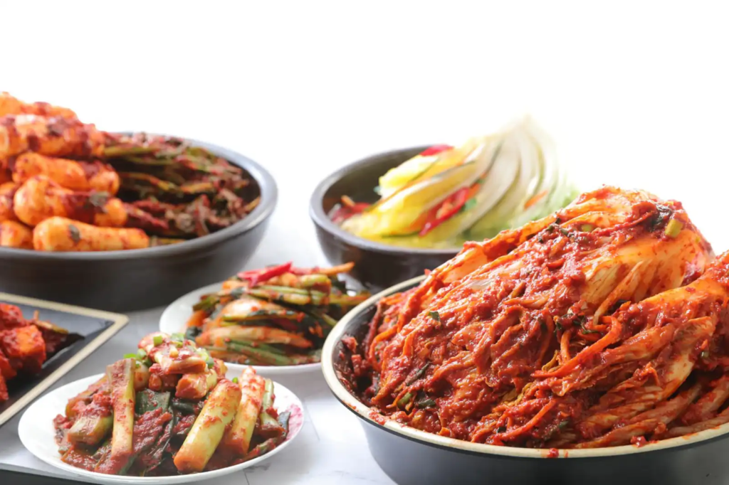 Korean Kimchi-A colorful assortment of traditional Korean Kimchi dishes, including napa cabbage Kimchi, green onion Kimchi, radish Kimchi, and another napa cabbage Kimchi without red pepper sauce, all arranged in bowls and plate on a bright surface