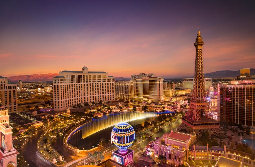 A vibrant aerial view of the Las Vegas Strip at sunset, featuring the Bellagio fountains and Eiffel Tower replica.