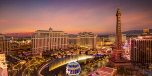 A vibrant aerial view of the Las Vegas Strip at sunset, featuring the Bellagio fountains and Eiffel Tower replica.