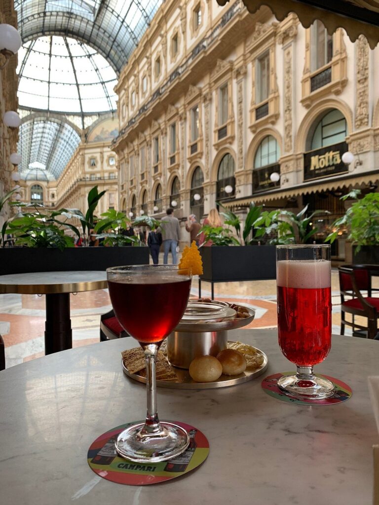 A table set with Campari-based aperitivo drinks and snacks at a cafe inside the elegant Galleria Vittorio Emanuele II in Milan.