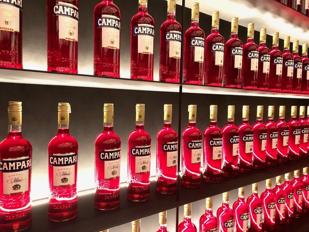 Rows of vibrant red Campari bottles lined up on illuminated shelves, showcasing the iconic Italian aperitif.