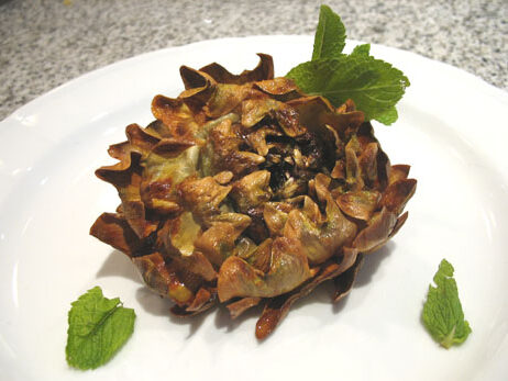 A single deep-fried Roman-Jewish artichoke, golden and crispy with curled petals, plated with fresh mint leaves on a white dish.