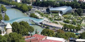 The Bridge of Peace stretching over the Kura River in Tbilisi, Georgia, with Rike Park and the modern tubular concert hall in the background — a symbolic view of East meets West.