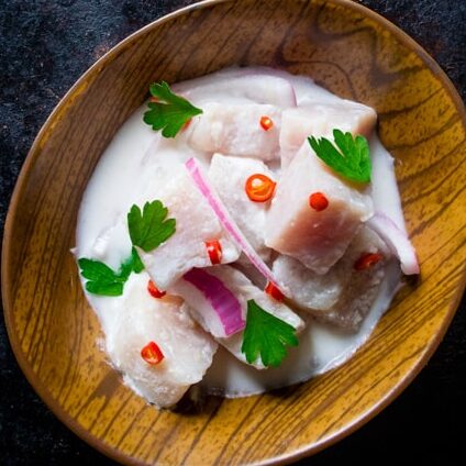 Filipino kinilaw made with diced fish in coconut milk, garnished with red chili, onions, and parsley in a wooden bowl.