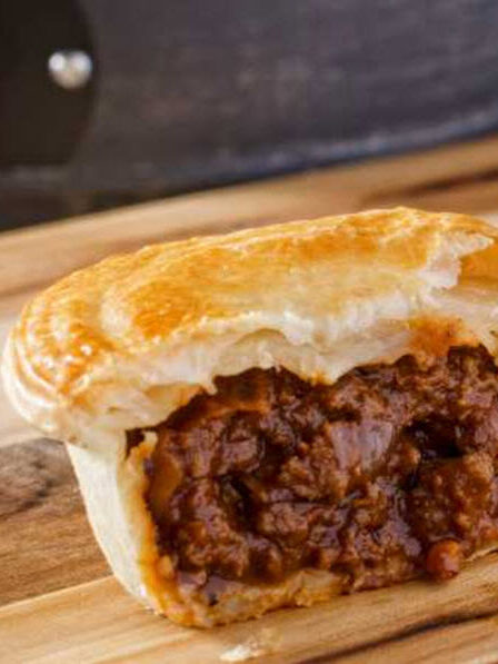 Golden-crusted meat pie filled with slow-cooked brisket on a wooden board at a Sydney bakery.