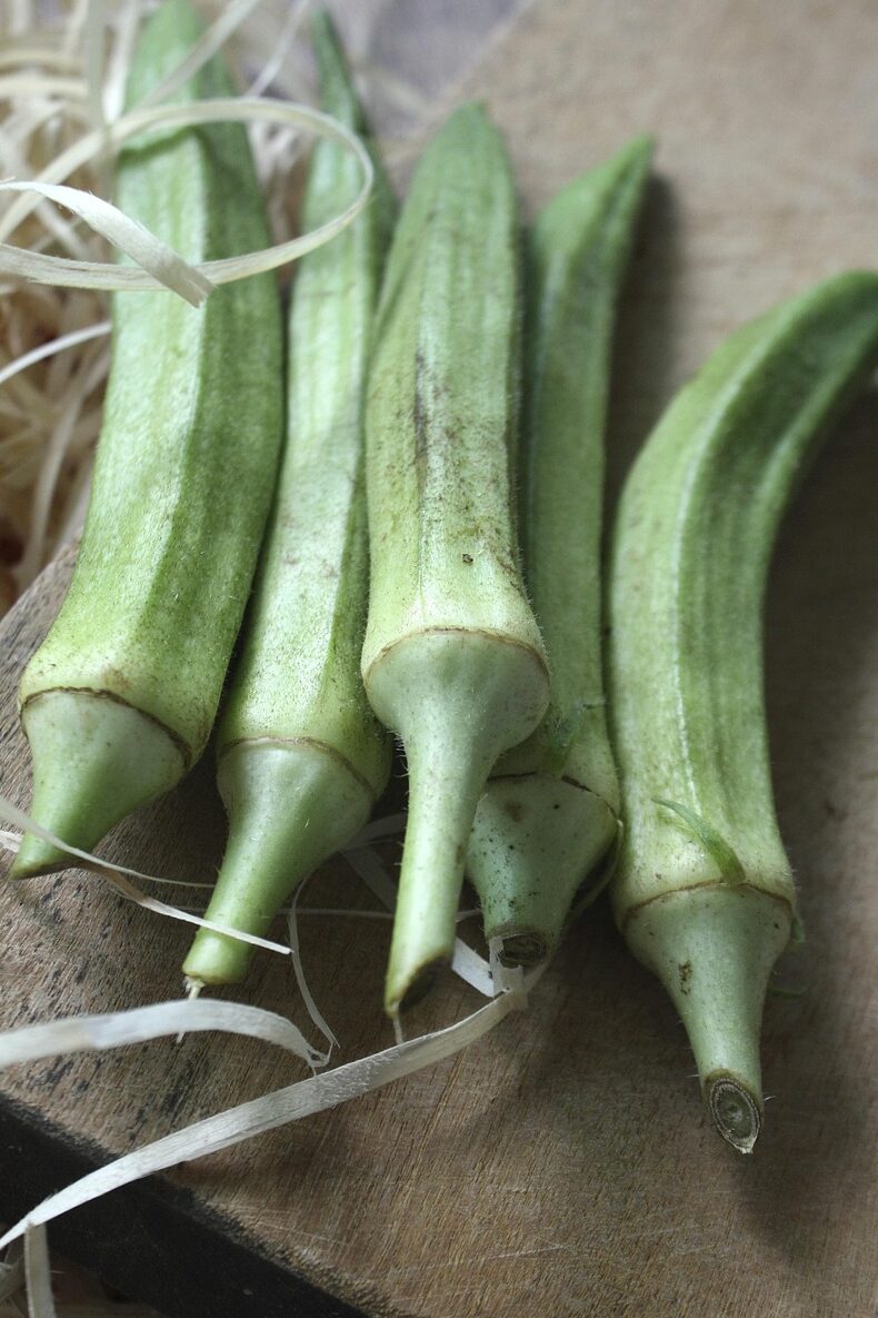 Fresh green okra pods on a wooden surface — a West African vegetable central to gumbo and it linked to traditional American American food.