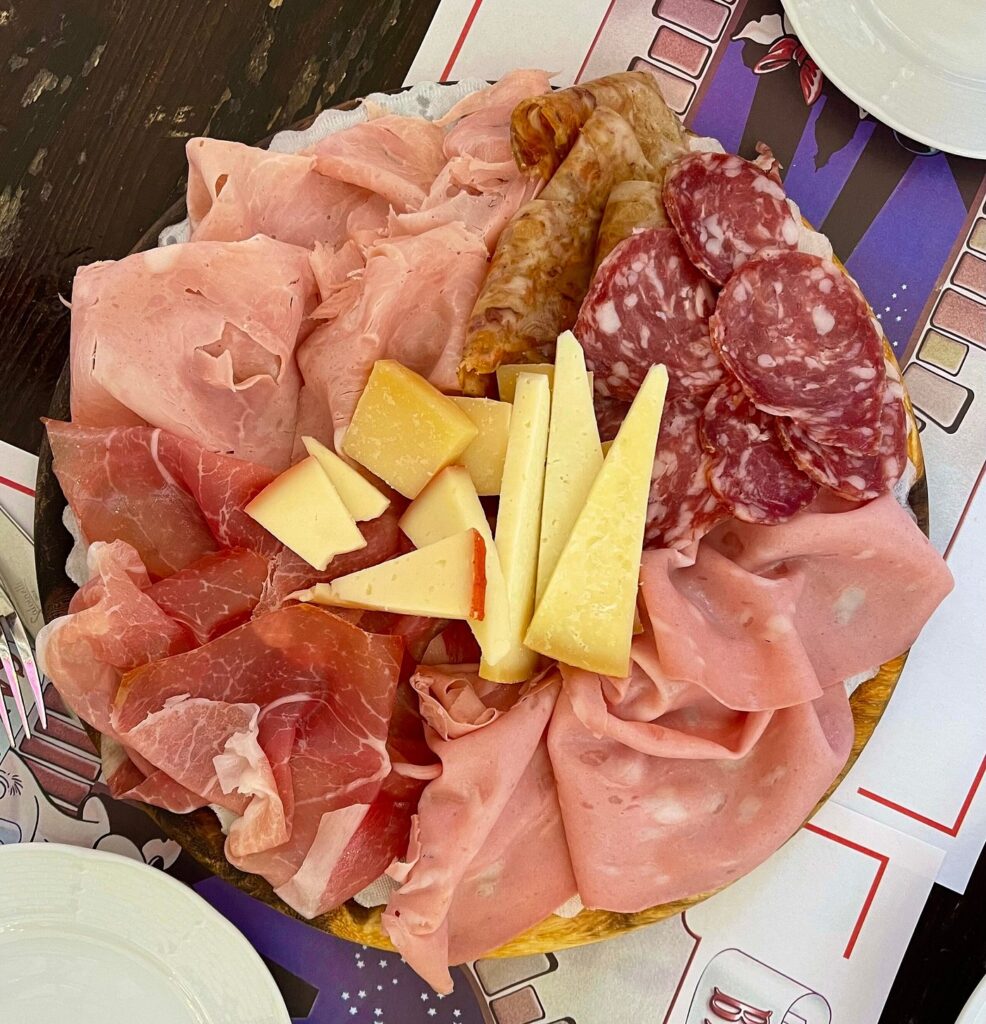 A traditional Italian charcuterie board featuring slices of mortadella, prosciutto, salami, and various aged cheeses, served on a rustic table in Bologna.
