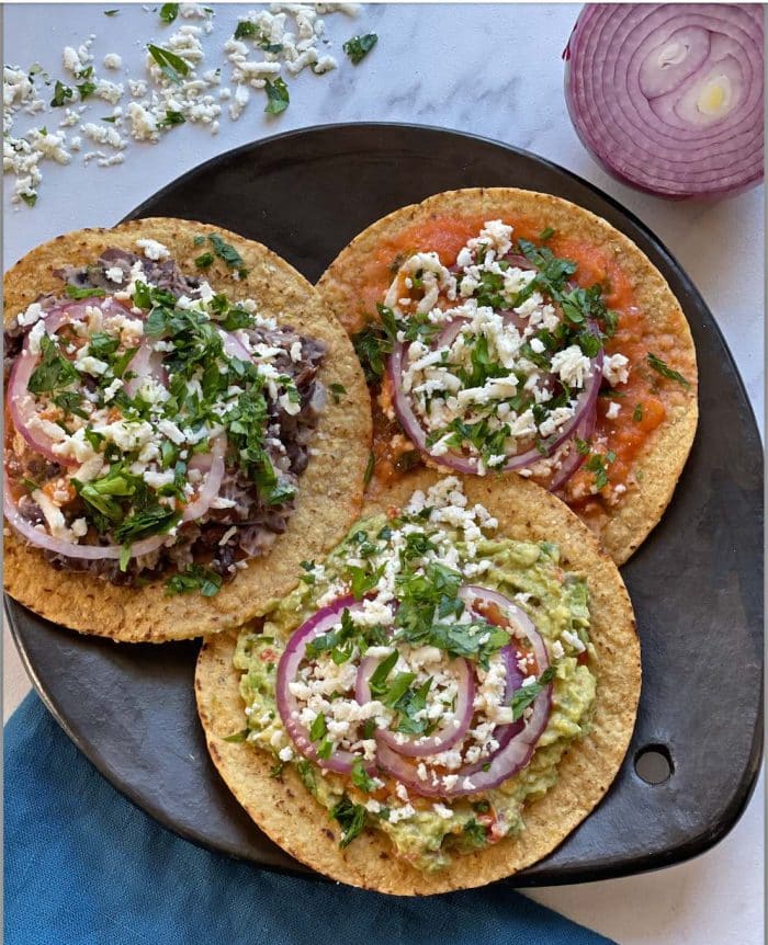 Traditional Guatemalan tostada topped with black beans, cheese, and fresh vegetables on a rustic table setting.