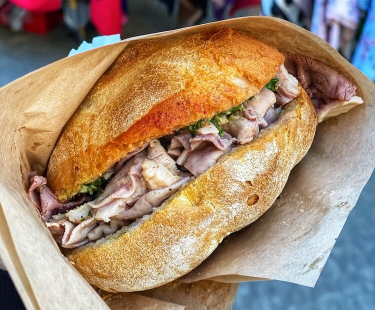 Close‑up of a classic Florentine Lampredotto sandwich: slow‑cooked cow’s stomach in a crusty roll, topped with fresh green sauce, street‑food style.
