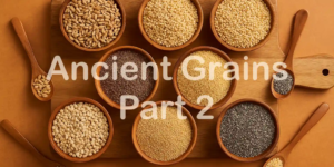 Assorted ancient grains including farro, chia, millet, and sorghum displayed in round wooden bowls on a wooden cutting board, with wooden spoons holding small portions, set against a warm-toned background.