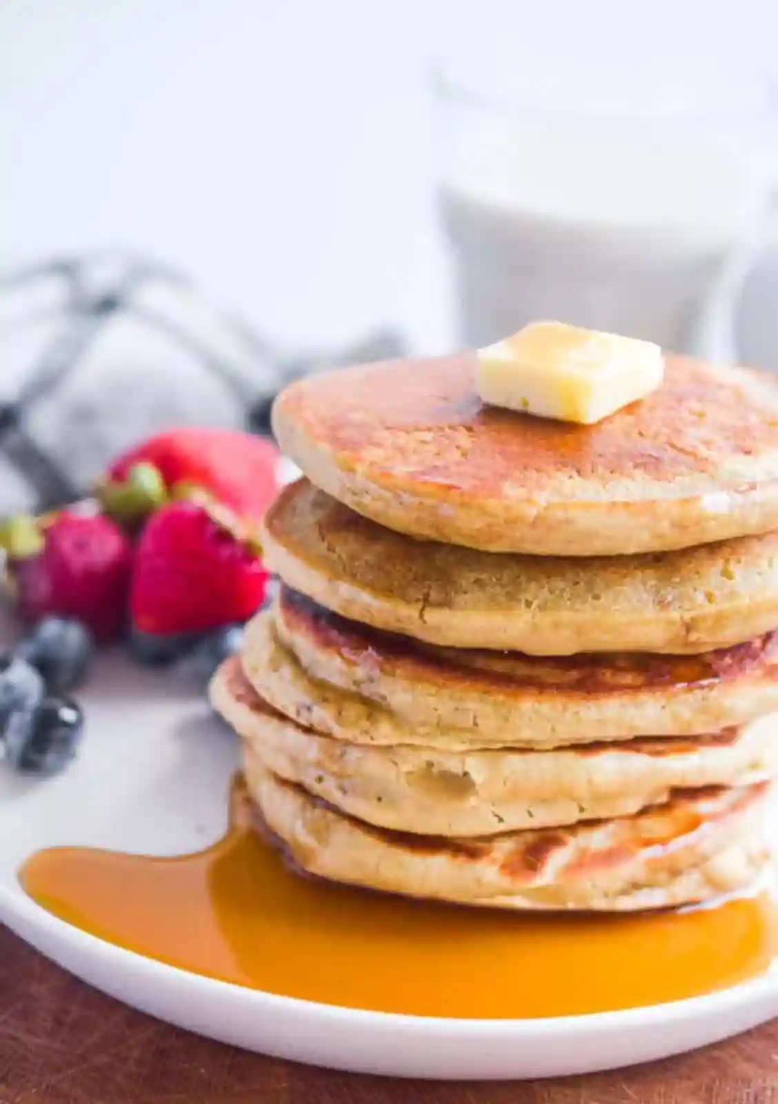A stack of golden ancient grain pancakes topped with butter and maple syrup, served with fresh berries.