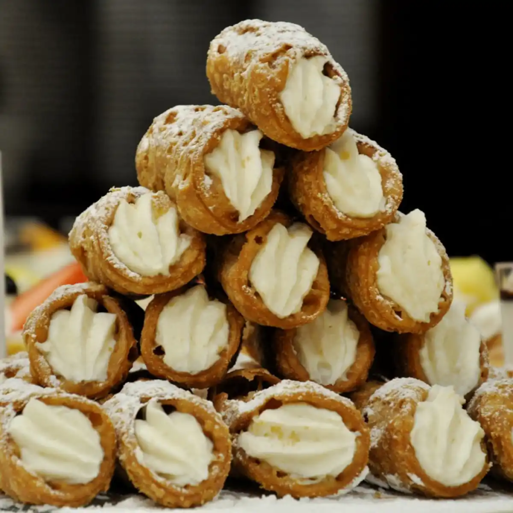 A pyramid stack of Sicilian cannoli filled with sweet ricotta cream and dusted with powdered sugar.