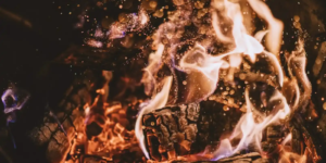 Glowing embers and swirling flames rising from a wood fire, capturing the warmth and ritual of traditional fire cooking.