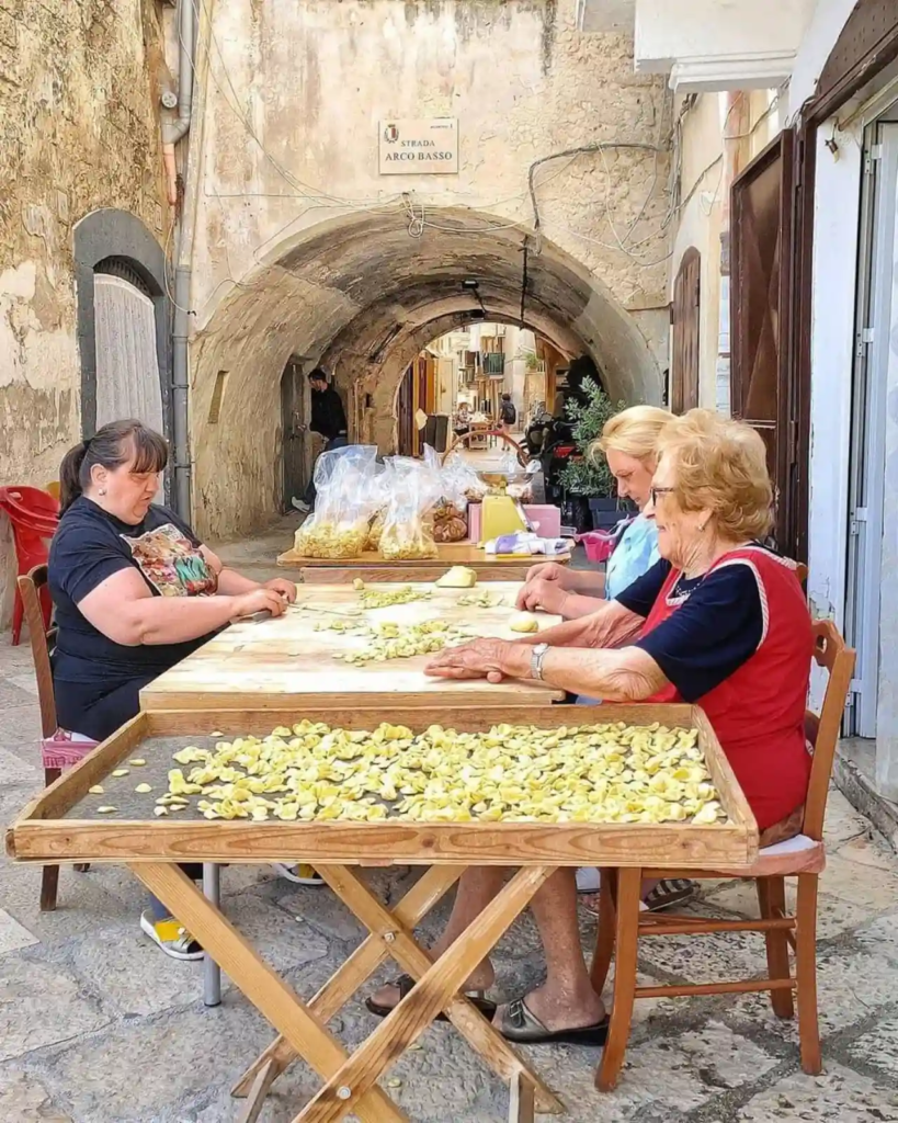 Elderly women making orecchiette pasta by hand in Bari’s Arco Basso street, Italy