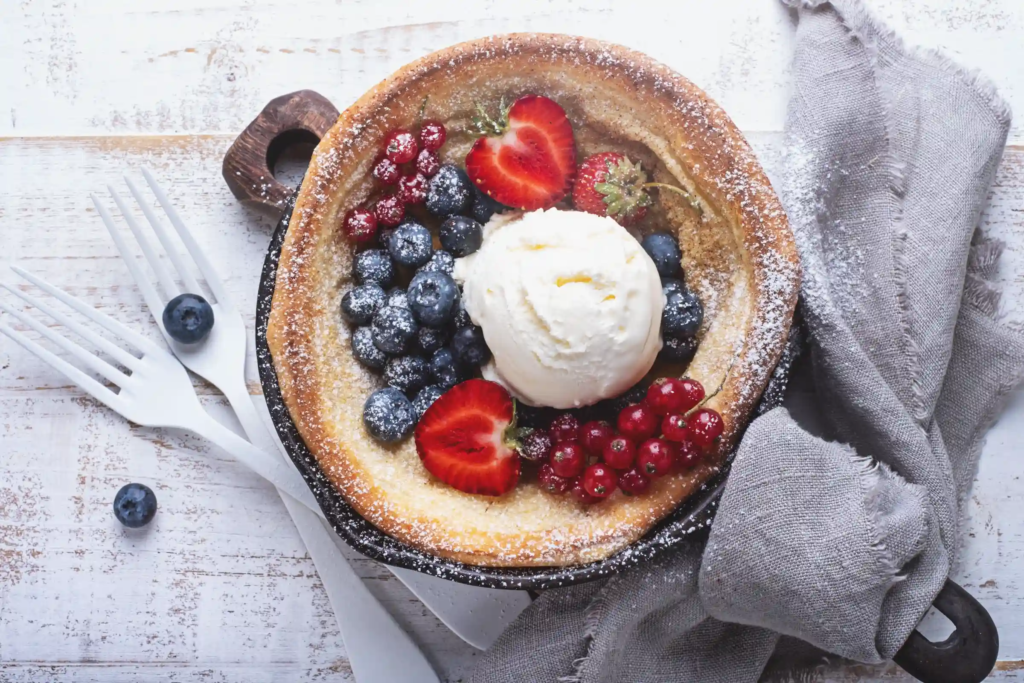 Fruit-covered Dutch pancake topped with vanilla ice cream and powdered sugar — a classic sugar-heavy breakfast that looks inviting but may spike blood sugar.