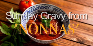 A bowl of tomato-based Sunday Gravy on a wooden table with herbs and tomato garnish