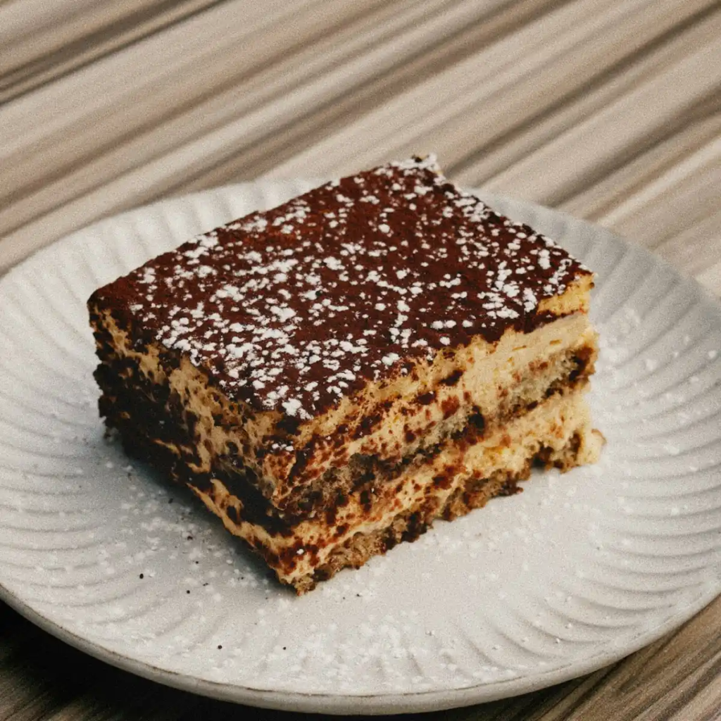 A slice of traditional Italian tiramisu with layers of espresso-soaked ladyfingers and mascarpone cream, dusted with cocoa powder.