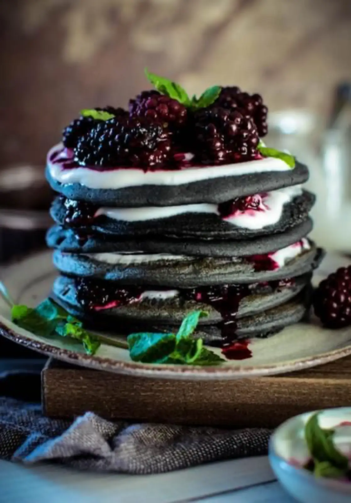 Stack of black charcoal pancakes with blackberry compote and mint
