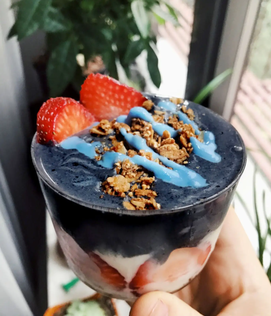 Charcoal yogurt parfait with strawberries, granola, and blue drizzle