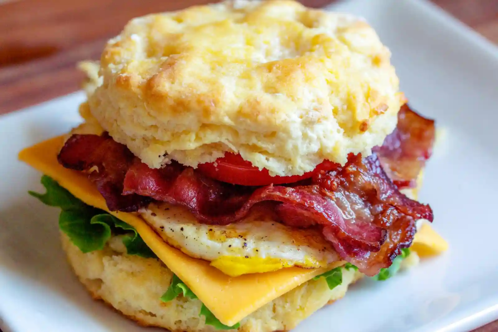 A bacon, egg, cheese, and tomato sandwich on a fluffy biscuit.
