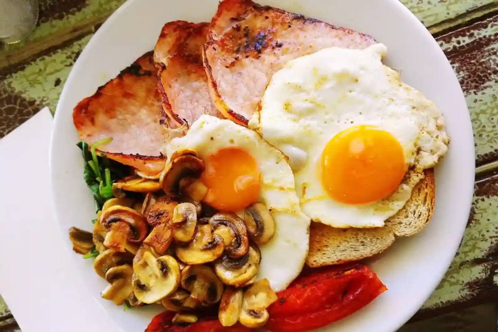 A hearty breakfast plate with crispy bacon, sunny-side-up eggs, sautéed mushrooms, and toast.