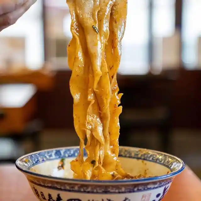 Wide hand-pulled Biang Biang noodles lifted from a bowl.