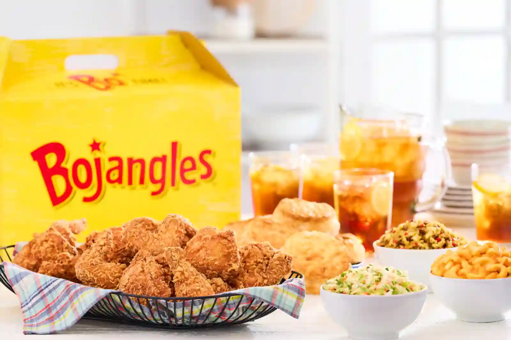 Bojangles family meal with a basket of fried chicken, biscuits, sides, and iced sweet tea beside a large yellow Bojangles box.