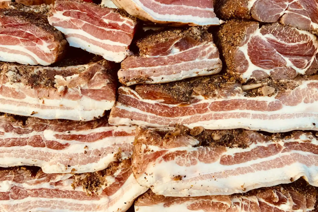 Close-up of cured pork belly slices stacked together, showing layers of meat and fat with seasoning.