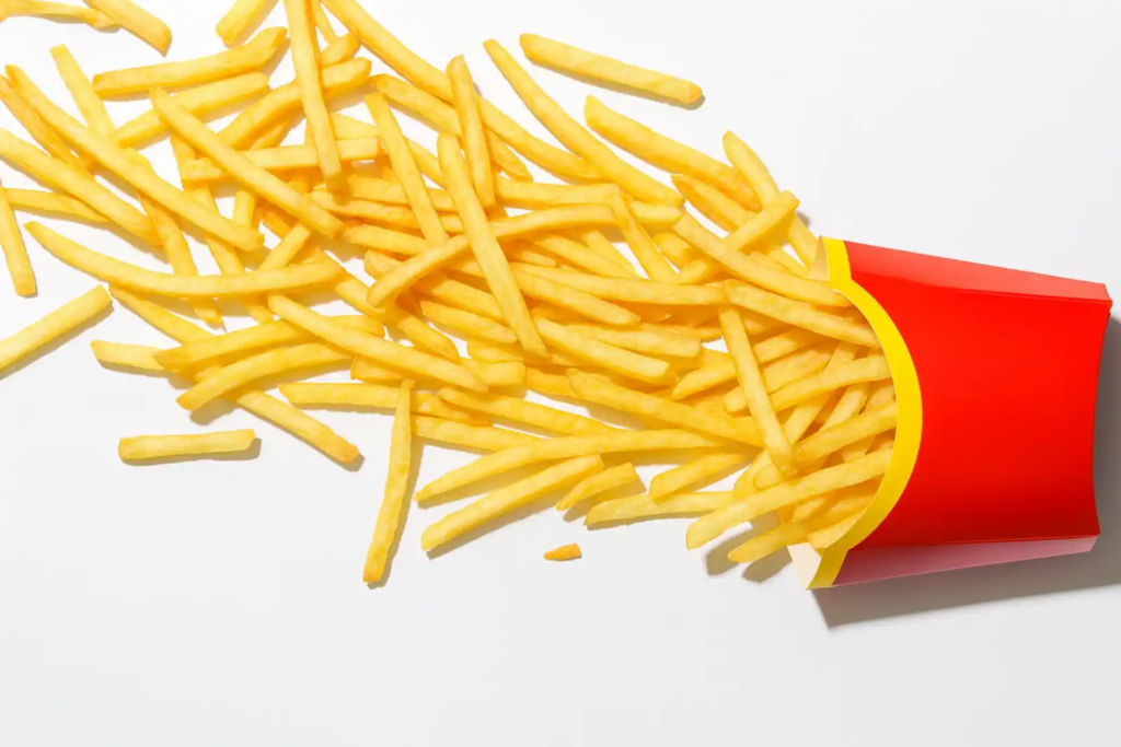 A red paper container of French fries tipped over, spilling golden fries across a clean white background.