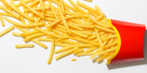 A red paper container of French fries tipped over, spilling golden fries across a clean white background.
