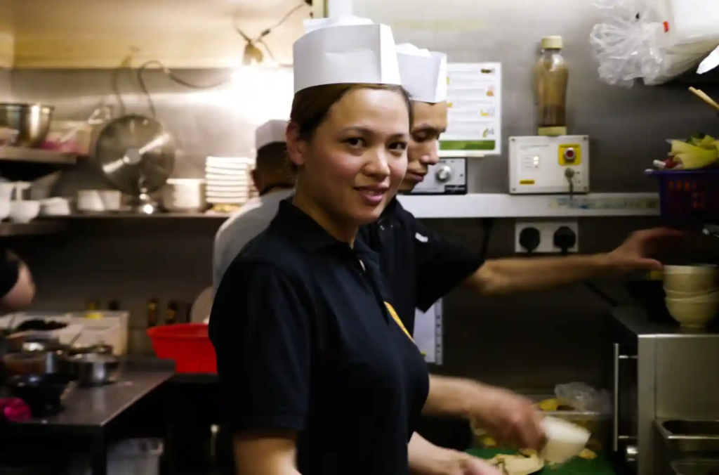 Chef Guirong Wei smiling in the kitchen while preparing food.