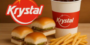 Krystal sliders with pickles and onions, fries, and an iced drink on a wooden surface, with the red Krystal logo.