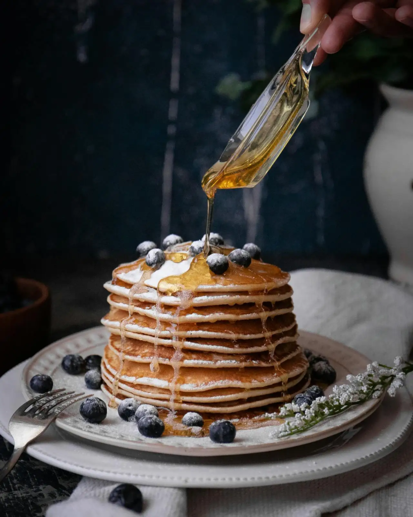Warm maple syrup drizzled over a tall stack of blueberry pancakes.