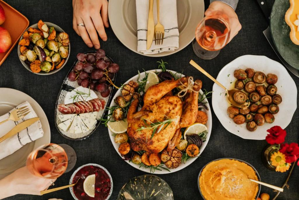 Table spread with roasted chicken, vegetables, cheese, grapes, and wine.