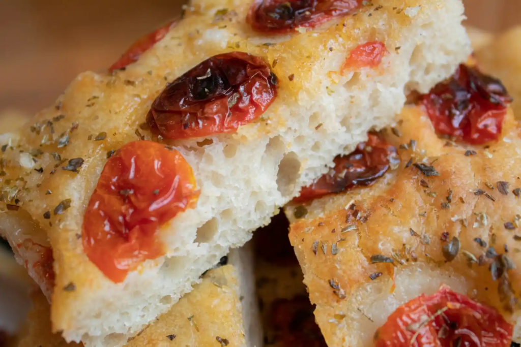 Close-up of focaccia topped with roasted cherry tomatoes and herbs, showcasing a light, airy crumb.