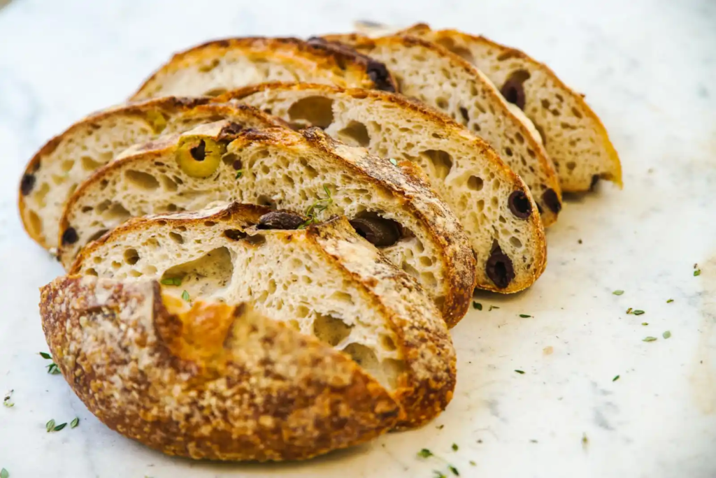 Slices of olive sourdough bread showing a golden crust and airy interior with green and black olives.