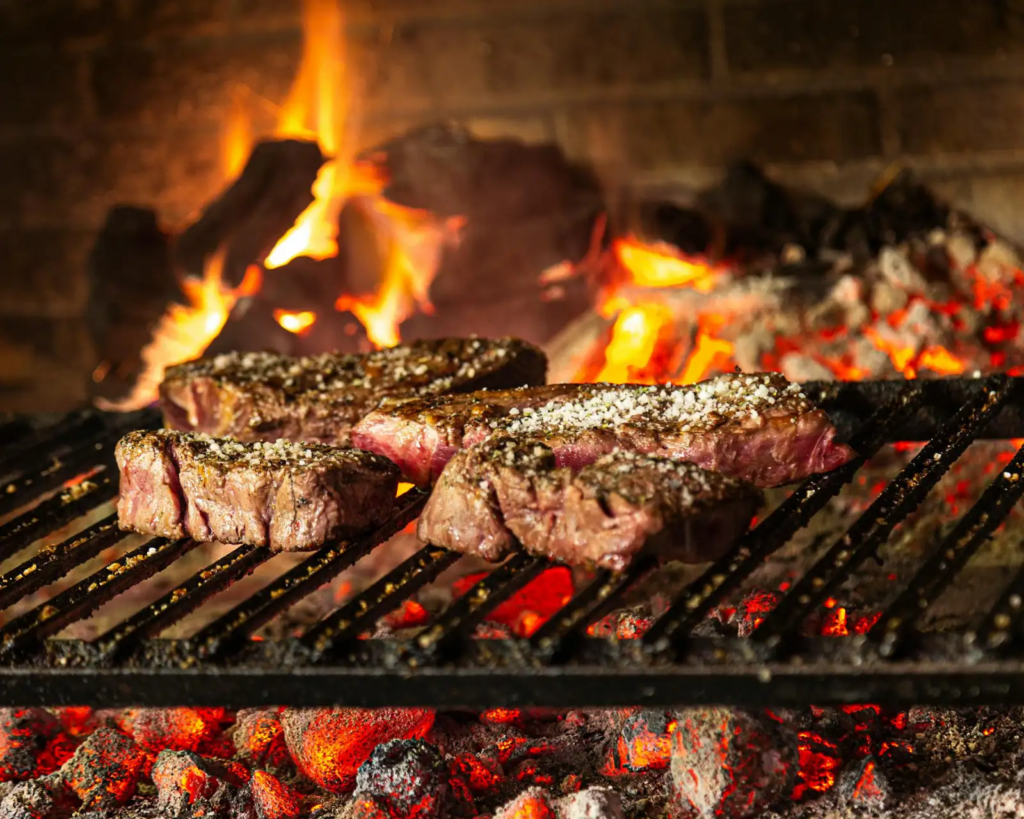 Steaks grilling over hot coals with visible flames.