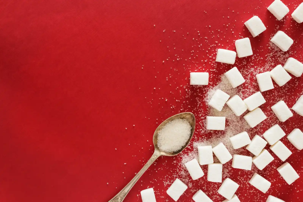 White sugar cubes and granulated sugar scattered on a red background with a spoon.