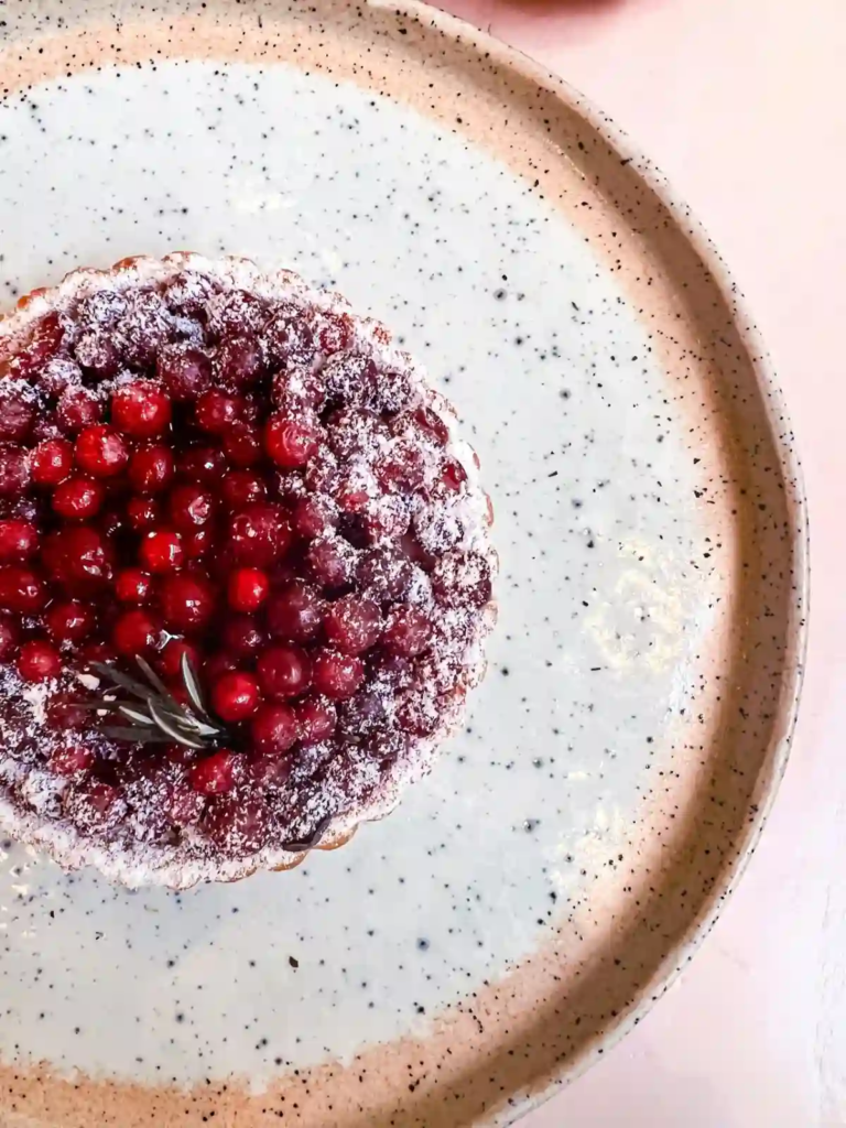 Cranberry tart dusted with powdered sugar on a speckled plate.