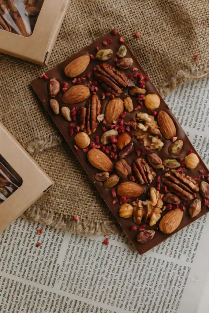 Dark chocolate bar topped with mixed nuts and dried cranberry pieces on burlap.