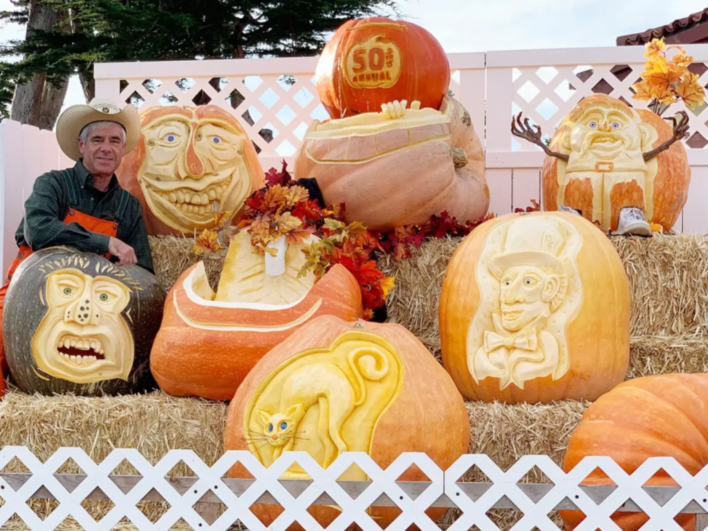 Pumpkin carving artist with a display of intricately carved pumpkins on hay bales.