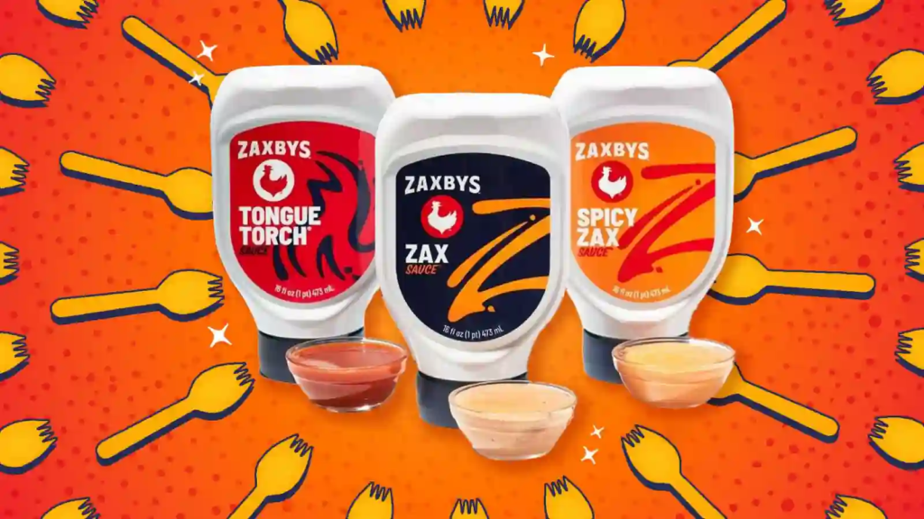 Original Zaxby’s — Tongue Torch, Zax Sauce, and Spicy Zax bottled sauces with dipping cups on an orange fork-pattern background.
